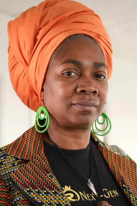 Photo of Torkwase Holmes by Dreph, in orange headscarf, green earrings and colourful jacket.